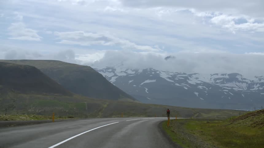 A man rides a bike on a road through a mountainous region