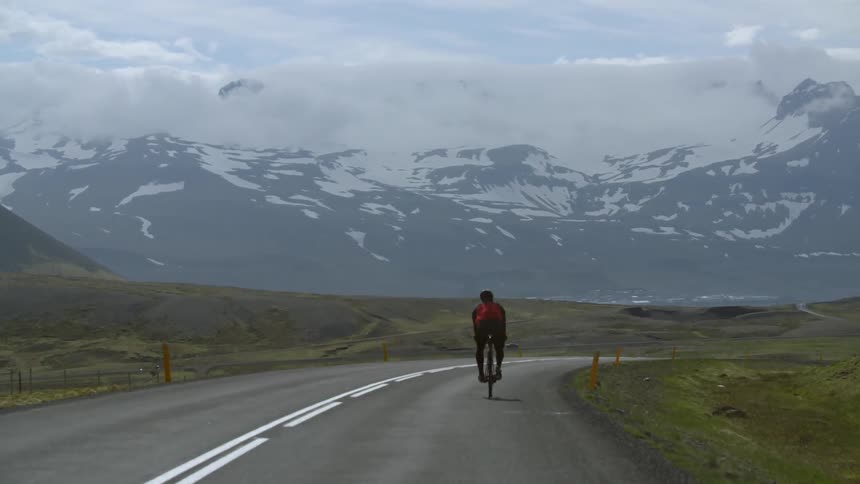 A cyclist rides his bike towards a snow covered mountain