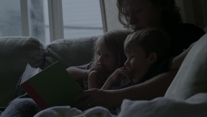 A woman and children read a book on the couch