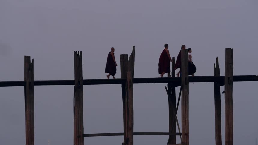People and monks walking over wooden bridge as a seagull flies by