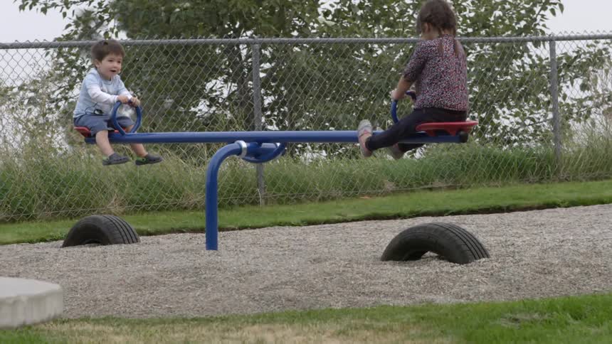 A boy and girl play on a seesaw