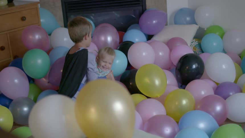 Two kids are playing amidst balloons