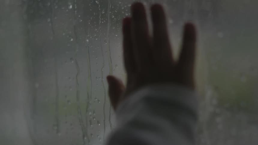 Small hand on a windowpane while raining outside