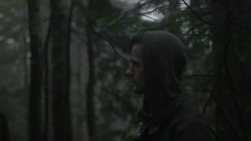 Hooded man walking through a dark forest