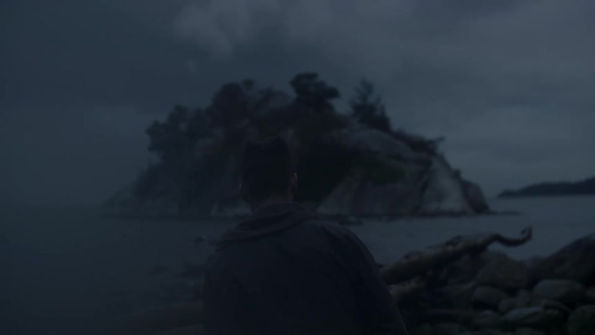 A man walks down a rocky beach at dusk