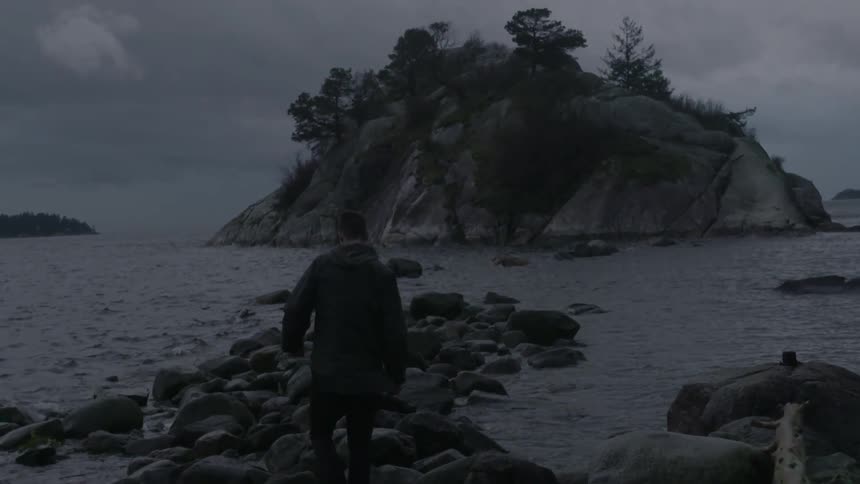 At dusk, a person walks out along some rocks that form a small peninsula into the water