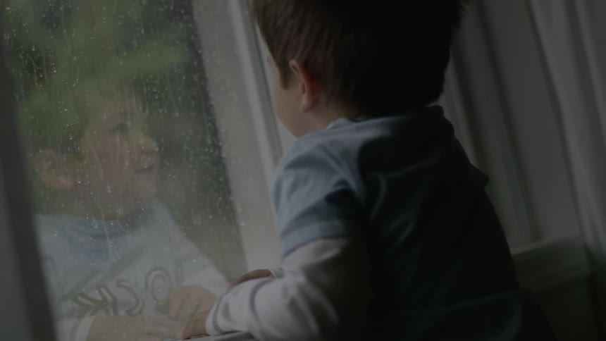 Little boy looking out the window watching the rain