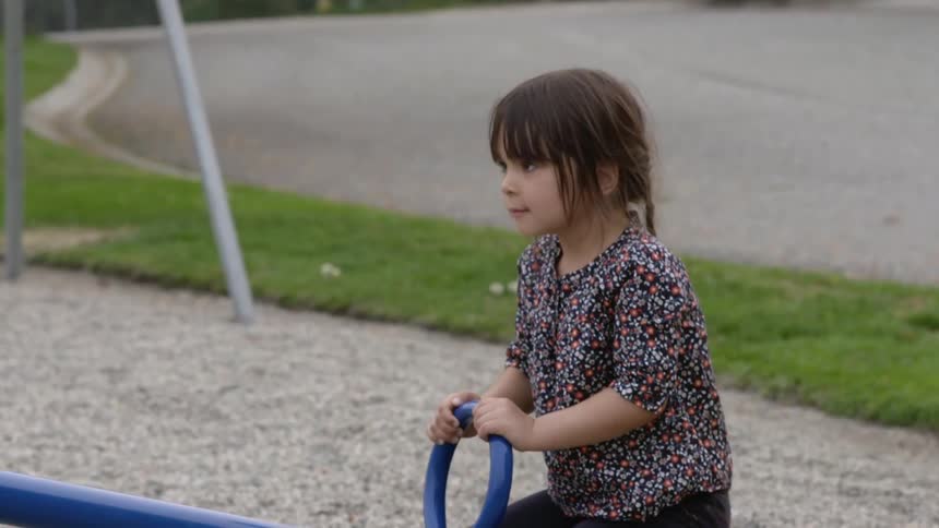 A young girl plays on a seesaw in a park during the day