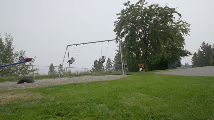 A view of two children swinging on a swing set in a small park