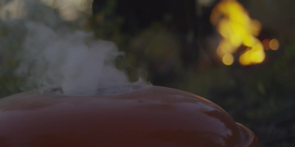 Smoke billows from a grill as a bonfire burns in the background