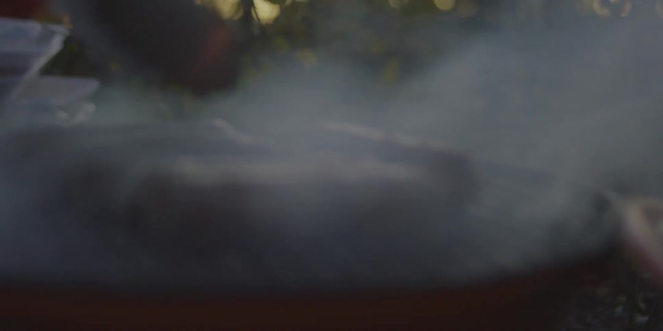 A person uses tongs to turn hot dogs on a bbq grill