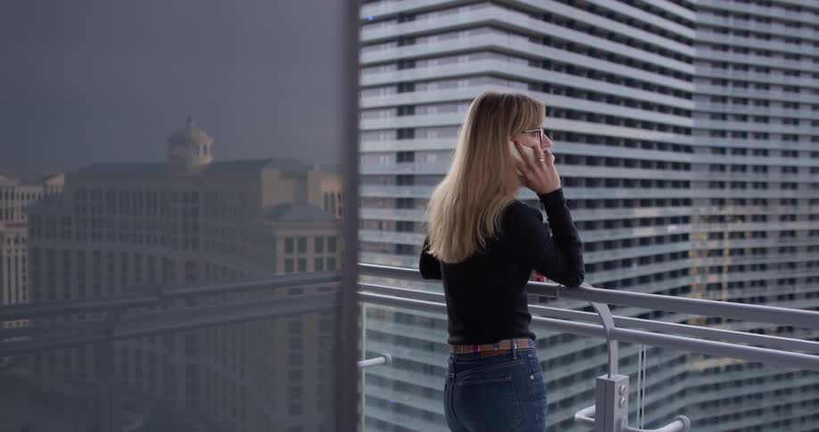 Woman is standing on balcony in city and talking on cell phone