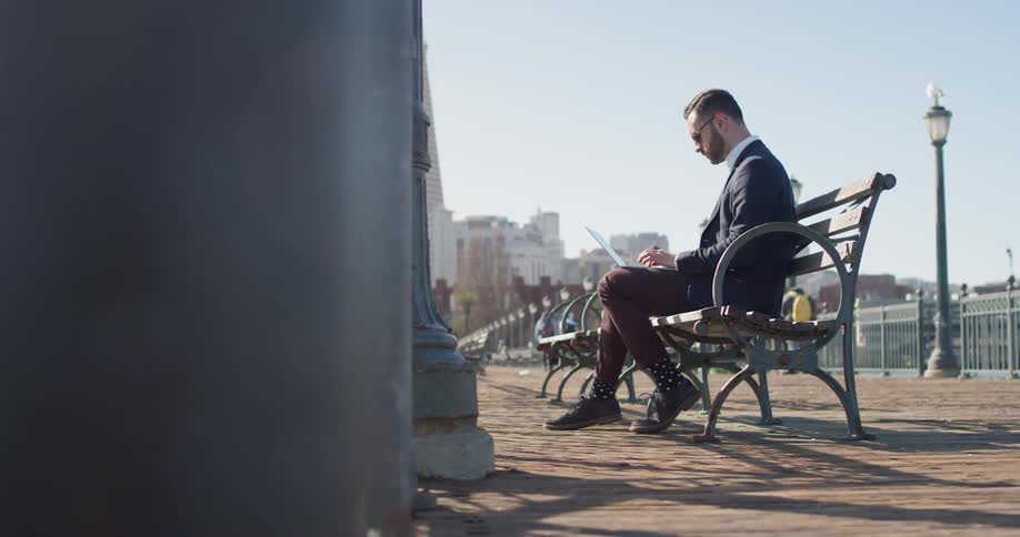 Man sits on a bench and works on a laptop on a sunny day
