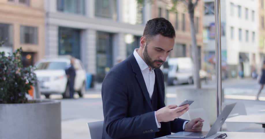 A business man uses his phone and laptop