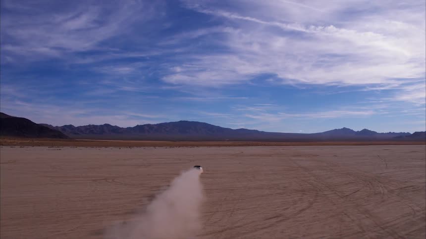 Car is driving fast on dirt flat land surrounded by mountains