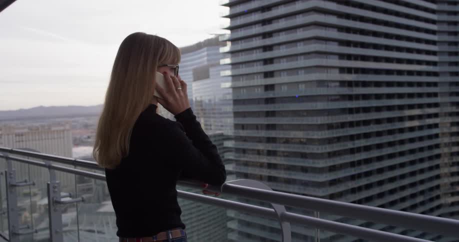 A woman talks on a phone on an apartment balcony