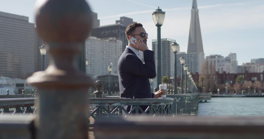 Man is talking on cell phone next to water in large city