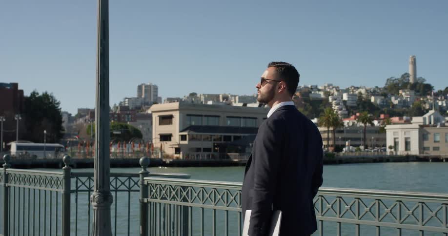 A man is holding a laptop as he walks on a pier in san francisco on a sunny day