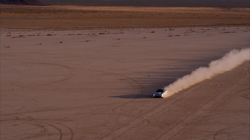 A car is leaving a dust trail as it speeds across a desert floor in daylight