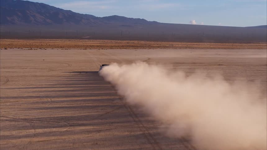 A car leaves a dust trail as it travels across a dirt field