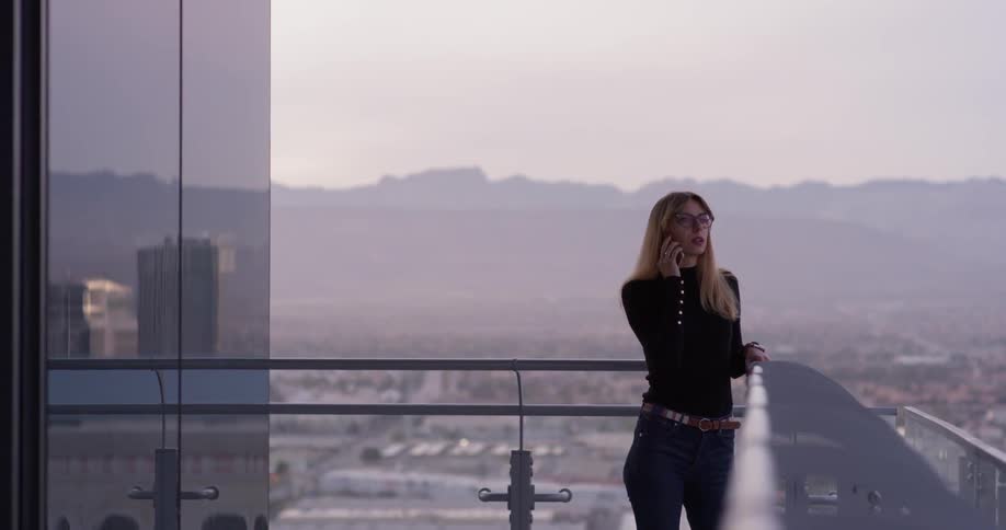 Woman talks on the phone while standing on a balcony overlooking the city
