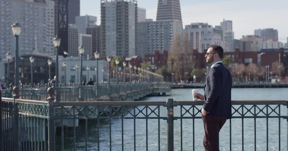 A man drinks coffee on a city pier