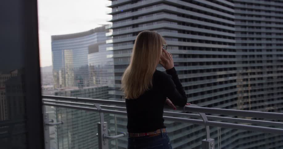 Woman is talking on cell phone on balcony in city