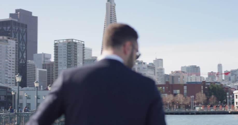 A man in a suit stands and looks out onto the water