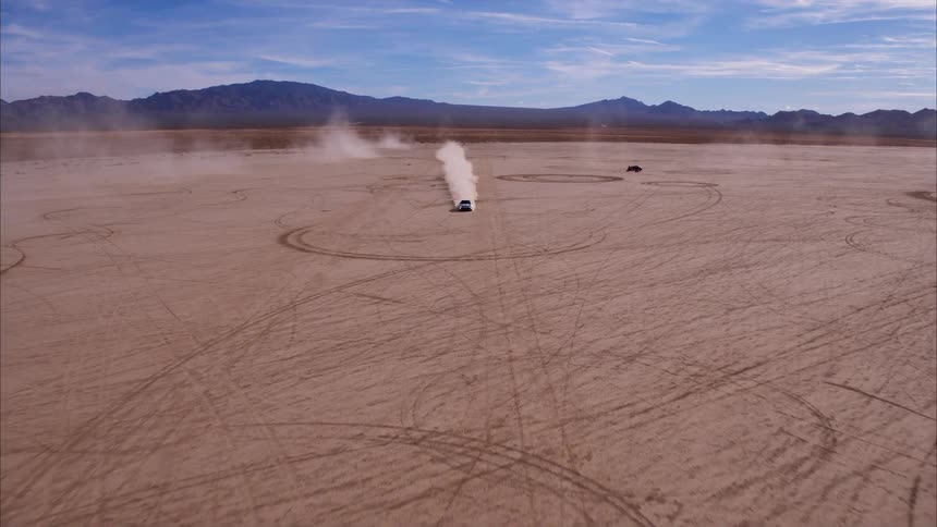 A car speeds across a dirt field surrounded by mountains