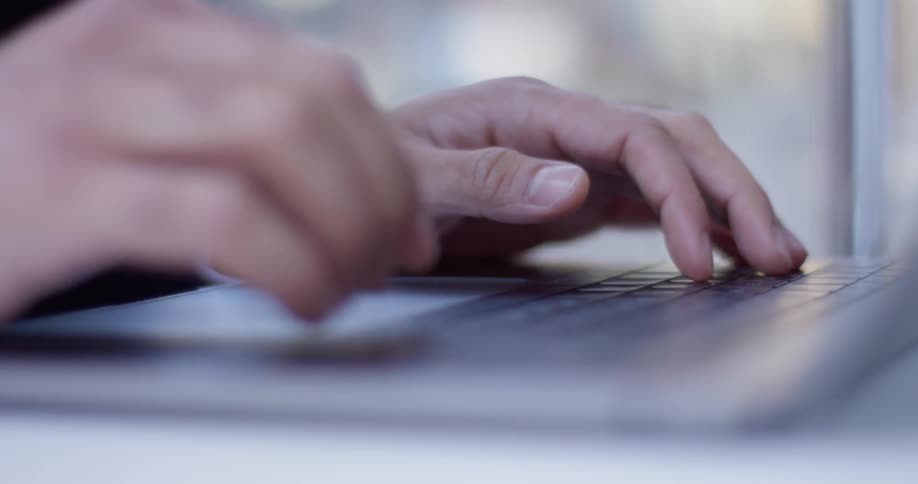 A man is typing on a laptop as he sits outside in a city in daylight