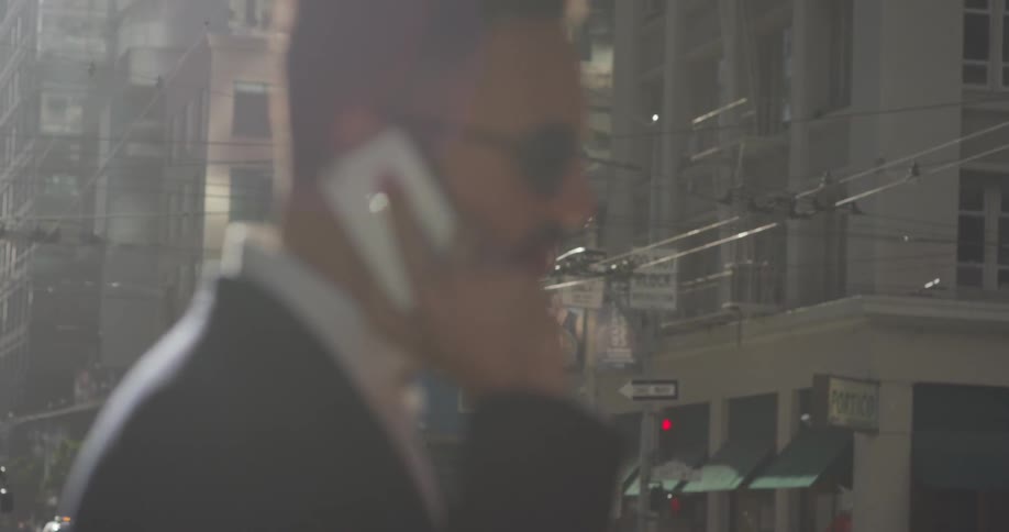 A man is standing outside in a city talking on a cellphone in daylight