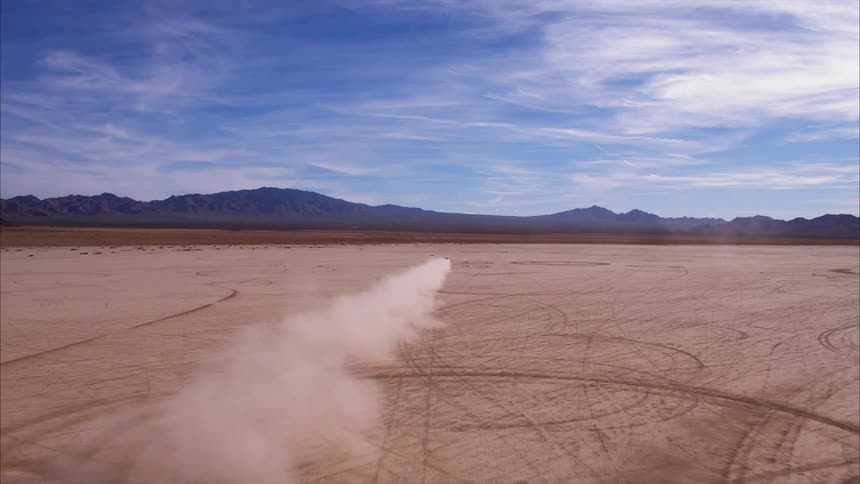 A car kicks up dirt as it speeds across the open land