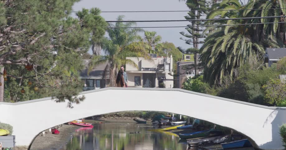 Man and woman walk over a bridge near the trees