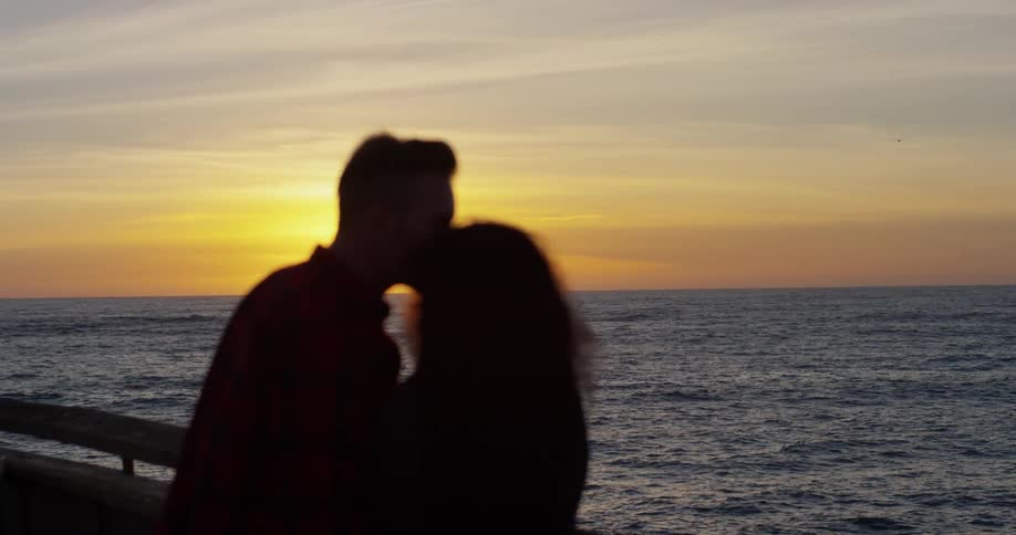 A man and woman kiss by the water