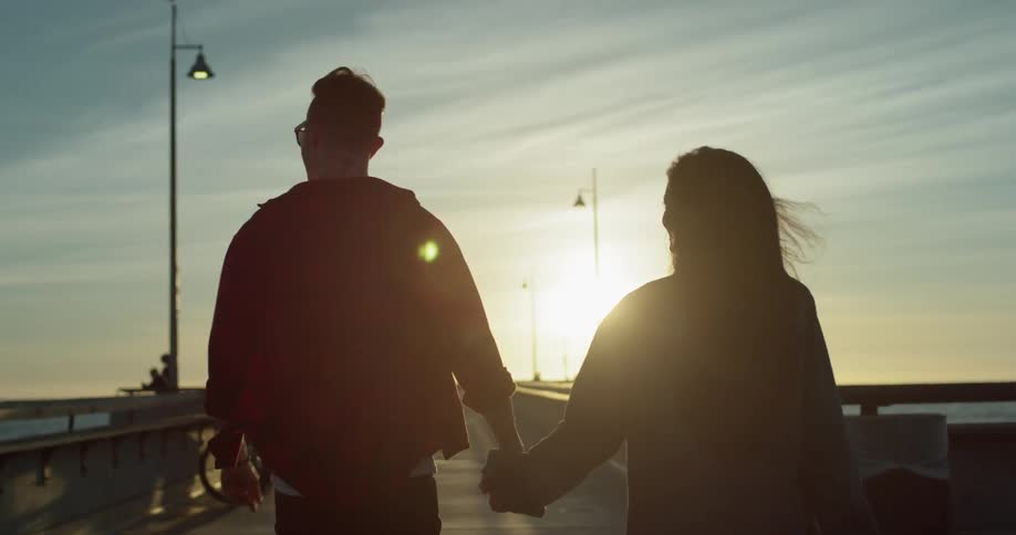 Man and woman hold hands and walk on a boardwalk on a sunny day