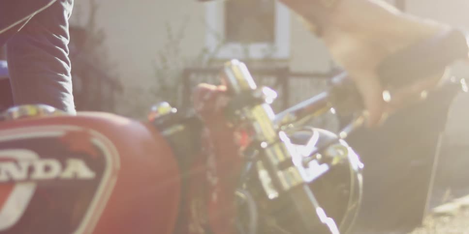 A man leans over a motorcycle in the sunlight