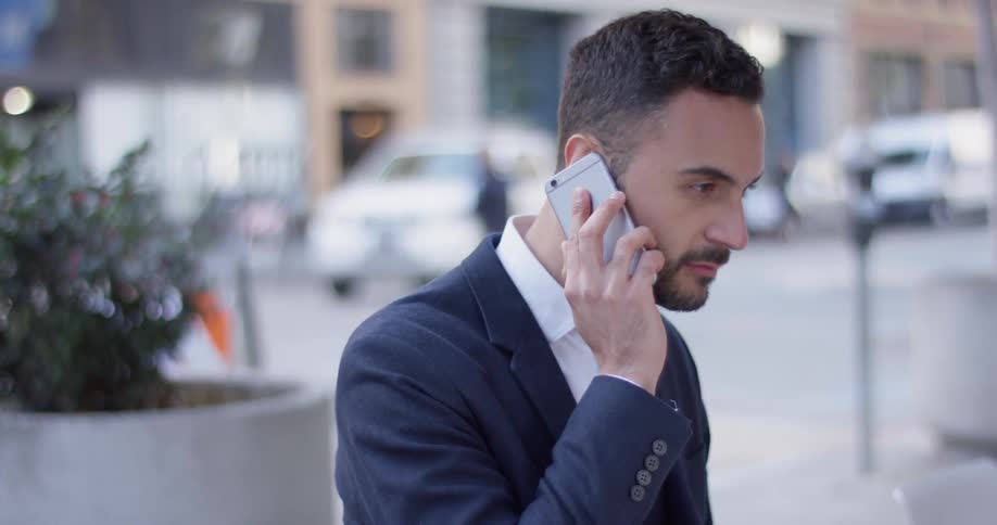 A man in a suit answers a phone call in a city