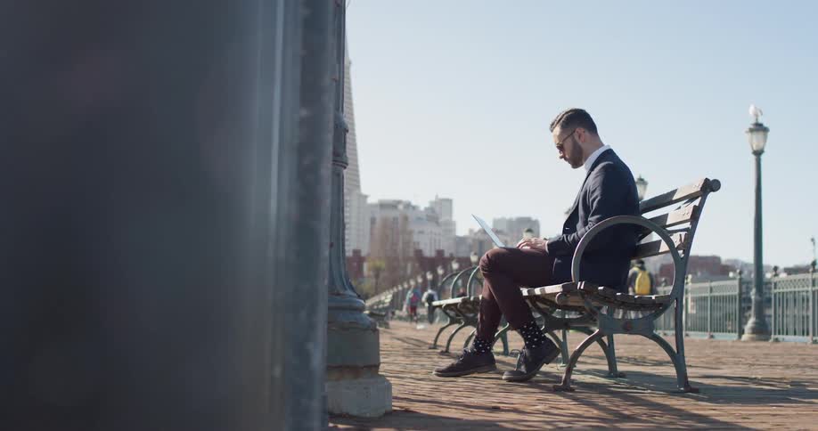 Man sits on a bench typing on a laptop