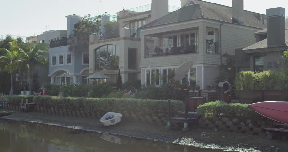 Two people walk past a row of houses next to a canal