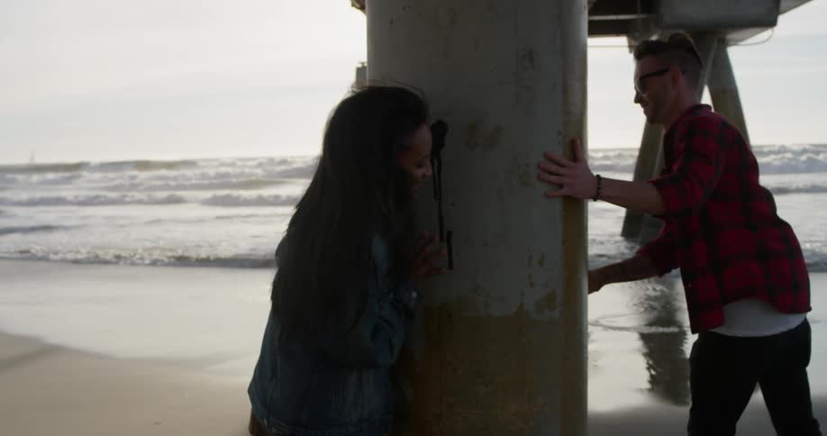 Man and woman chase each other around a large pillar by a body of water