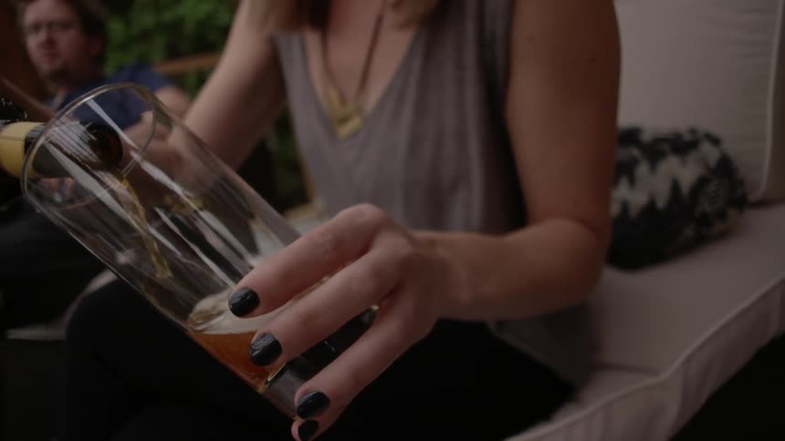 A woman wearing black nail polish pouring beer into a glass