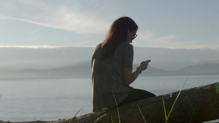 Woman looks at phone sitting on a log