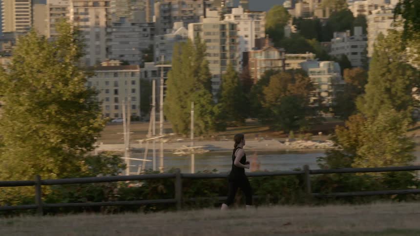 A woman runs in a park with a city in the background