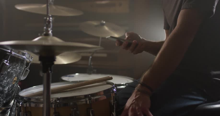 Man sits behind a drum set looking at his phone
