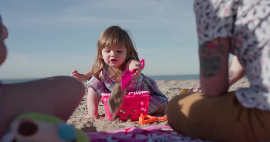 Young child shovels the sand at the beach as a man plays with a toy nearby