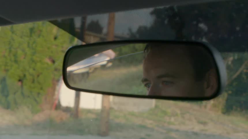 A man is seen reflected in his rear-view mirror as he drives along a neighborhood street