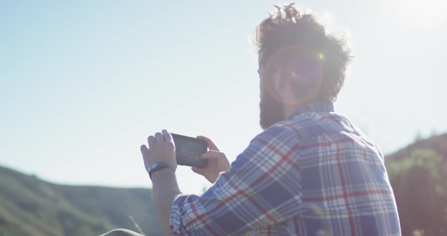 Man sits in the grass taking pictures of nature on a sunny day