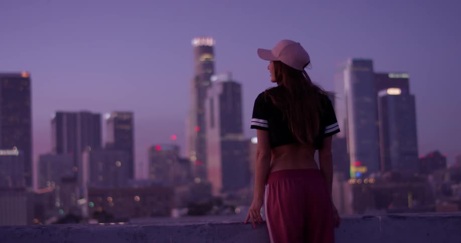 A woman is standing on a rooftop at dusk taking in an urban view