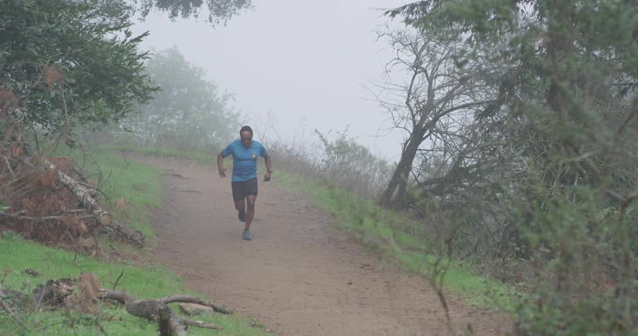A man jogs on a dirt trail on a foggy day