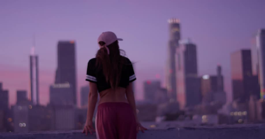 A woman is standing on a rooftop at dawn taking in an urban view